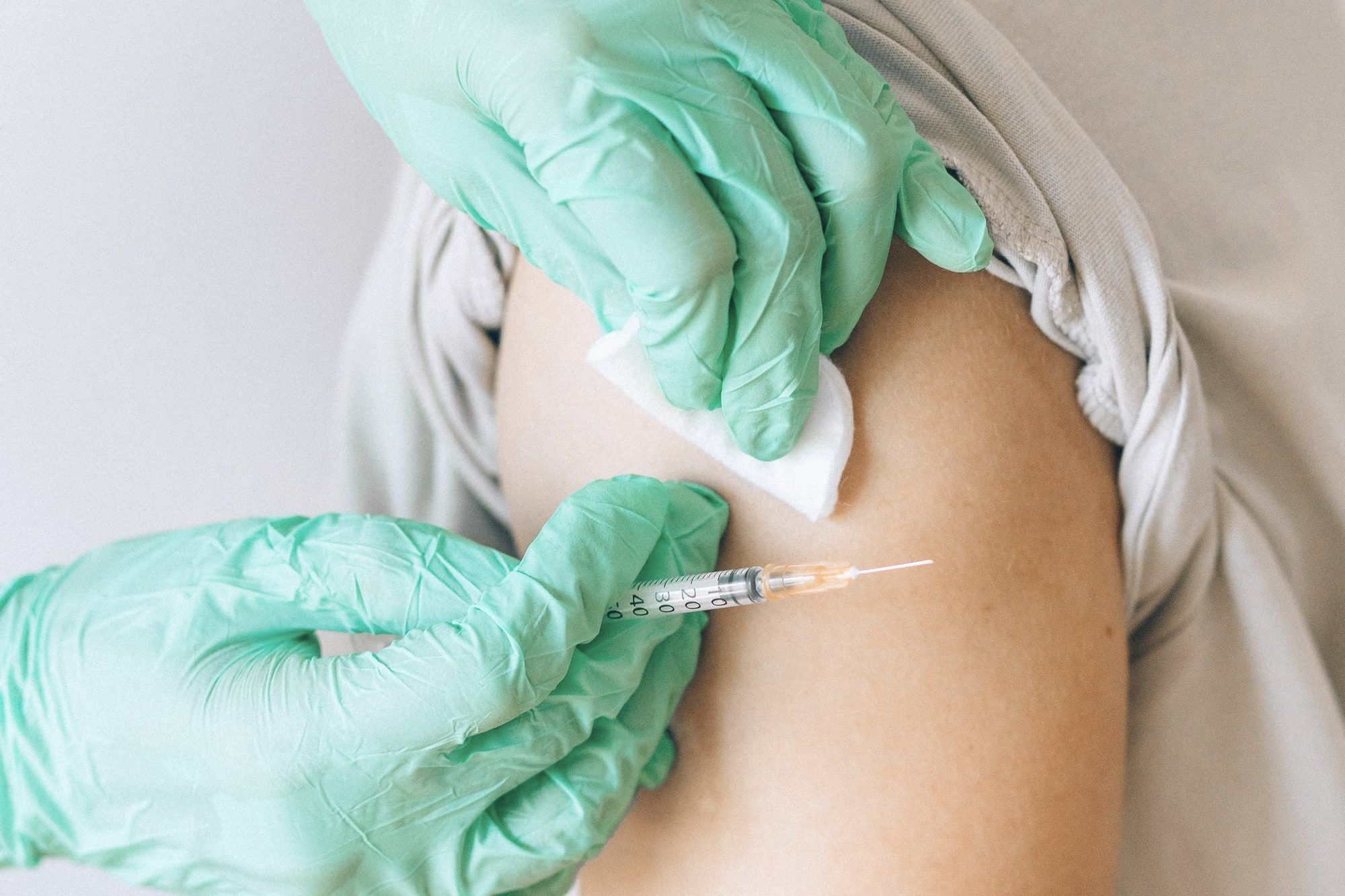 Ruke u medicinskim rukavicama daju injekciju u nadlakticu, uz vatu.
